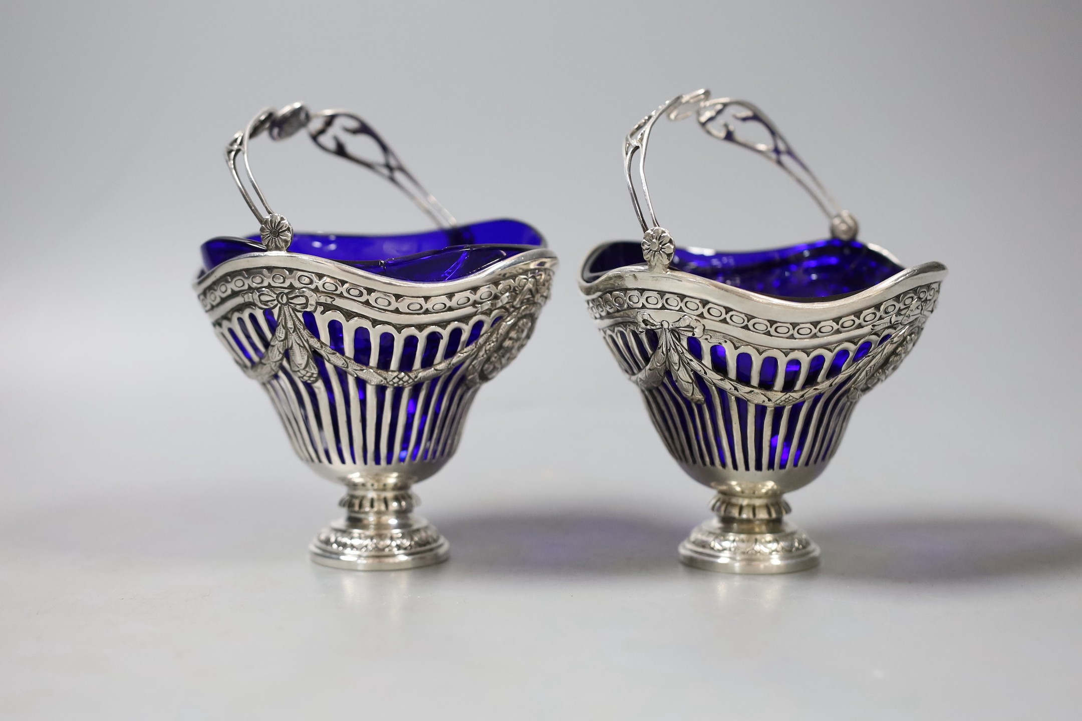 A pair of continental pierced white metal sugar baskets, with shaped blue glass liners, diameter 11.4cm.